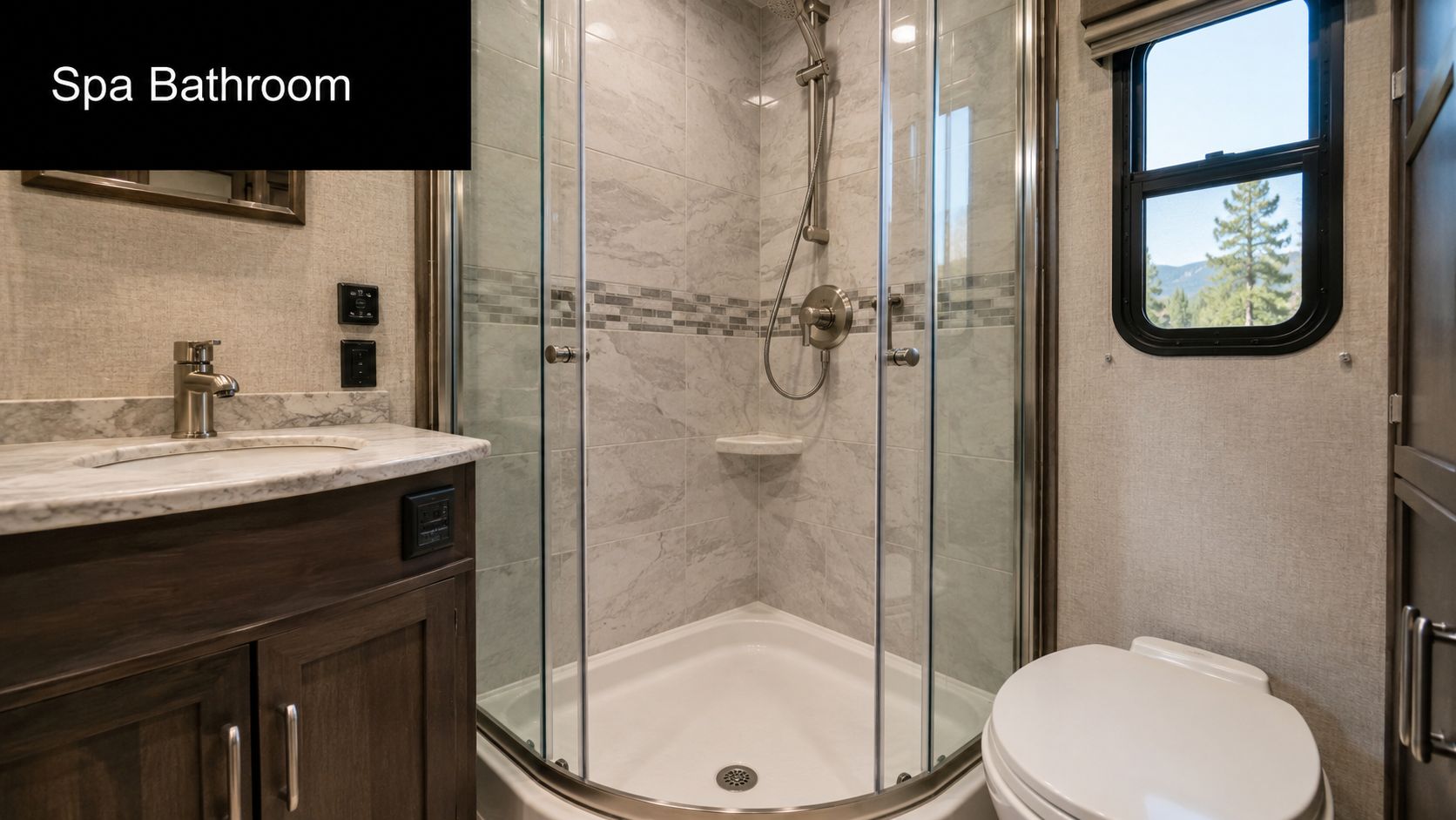 A clean and modern small spa bathroom inside an RV featuring a glass shower, vanity, and toilet.