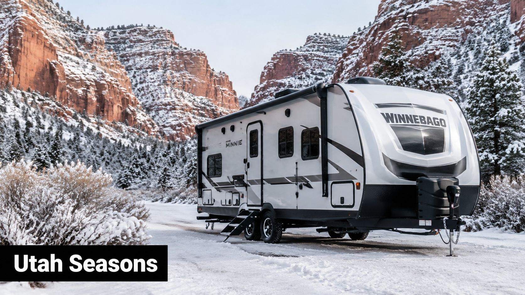 A modern Winnebago travel trailer parked in a snowy landscape surrounded by red rock cliffs in Utah.