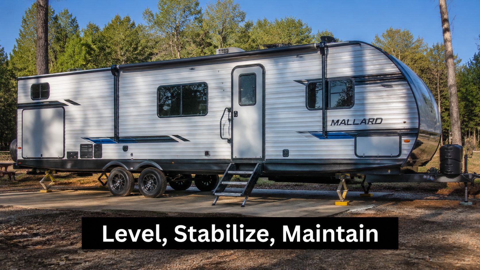 A silver Mallard travel trailer parked on a concrete pad with its stabilizer jacks extended.